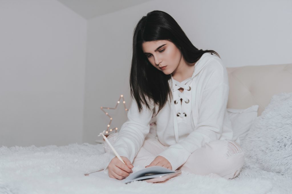 girl sitting on bed writing in planner notebook to set intentions